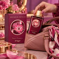 Zimaya Reverie Petals by Zimaya 100ml EDP Women — A woman's hand with dark red nails reaches for the gold cap of a deep red perfume bottle, next to its matching box, surrounded by dark red flowers and delicate white blossoms on a marble surface.