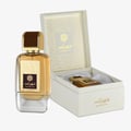 Ard Al Zaafaran Shahrazad Eau De Parfum — A white box with gold leaf pattern and a clear glass perfume bottle with gold accents and amber liquid, set against a white background. | Ard Al Zaafaran Shahrazad Eau De Parfum — Kotak putih dengan corak daun emas dan botol minyak wangi kaca jernih dengan aksen emas dan