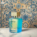 Lattafa Sheikh Al Shuyukh Supreme by Lattafa 100ml — A blue and green faceted glass perfume bottle with a gold textured cap sits next to its blue and light blue patterned box, which features an image of a man in traditional headwear. | Lattafa Sheikh Al Shuyukh Supreme by Lattafa 100ml — Botol kaca berfaset biru dan