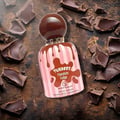 Grandeur Tubbees Chocolate Fudge — A perfume bottle with a chocolate-colored spherical cap and pink and white striped body, with chocolate drips cascading down. Next to it is the product box with the same design. | Grandeur Tubbees Chocolate Fudge — Botol minyak wangi dengan penutup bulat berwarna coklat dan badan