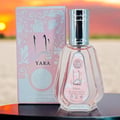 Ard Al Zaafaran Yara Eau De Parfum 50ml — Pink floral patterned box next to a faceted pale pink perfume bottle with a silver cap. | Ard Al Zaafaran Yara Eau De Parfum 50ml — Kotak bercorak bunga merah jambu di sebelah botol minyak wangi merah jambu pucat berfaset dengan penutup perak.