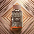 Zimaya Amber Is Great Eau De Parfum 100ml — A brown textured box with gold geometric art deco design stands next to a rectangular glass perfume bottle with a ribbed brown cap and gold geometric art deco design. The bottle contains amber-colored liquid. | Zimaya Amber Is Great Eau De Parfum 100ml — Kotak bertekstur