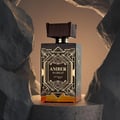 Zimaya Amber Is Great Eau De Parfum 100ml — A brown textured box with gold geometric art deco design stands next to a rectangular glass perfume bottle with a ribbed brown cap and gold geometric art deco design. The bottle contains amber-colored liquid. | Zimaya Amber Is Great Eau De Parfum 100ml — Kotak bertekstur