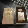 Zimaya Amber Is Great Eau De Parfum 100ml — A brown textured box with gold geometric art deco design stands next to a rectangular glass perfume bottle with a ribbed brown cap and gold geometric art deco design. The bottle contains amber-colored liquid. | Zimaya Amber Is Great Eau De Parfum 100ml — Kotak bertekstur